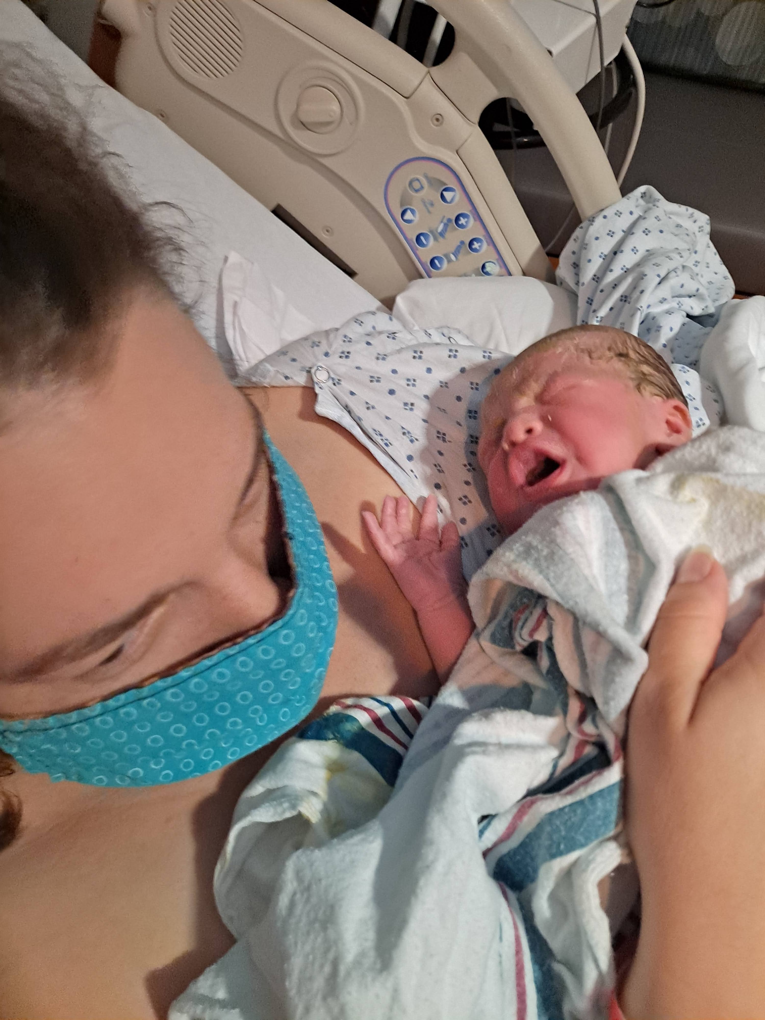 Woman in fabric mask holding a new baby in a hospital bed.