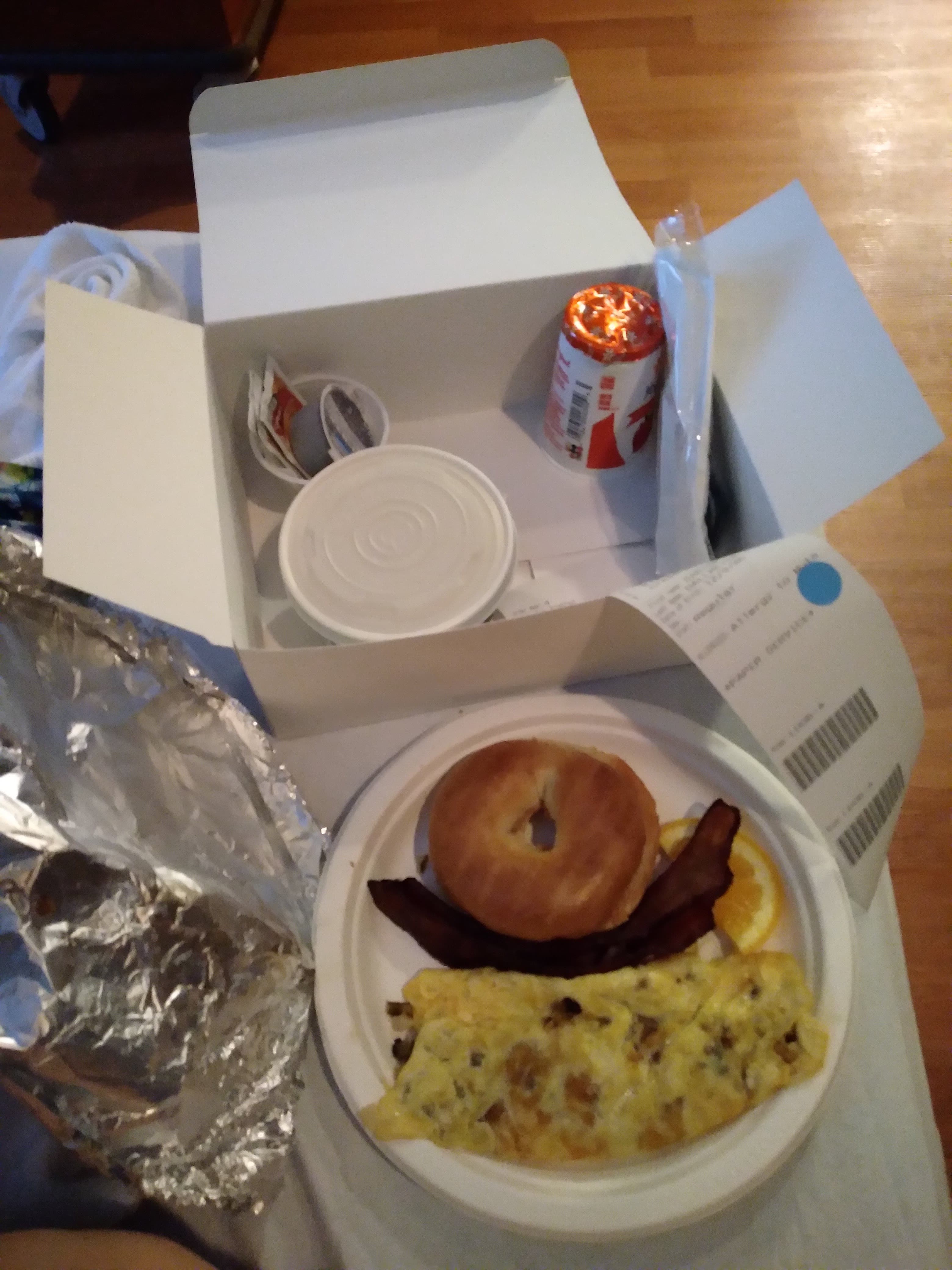 Box lunch containing yogurt. Paper plate with eggs bacon and a bagel