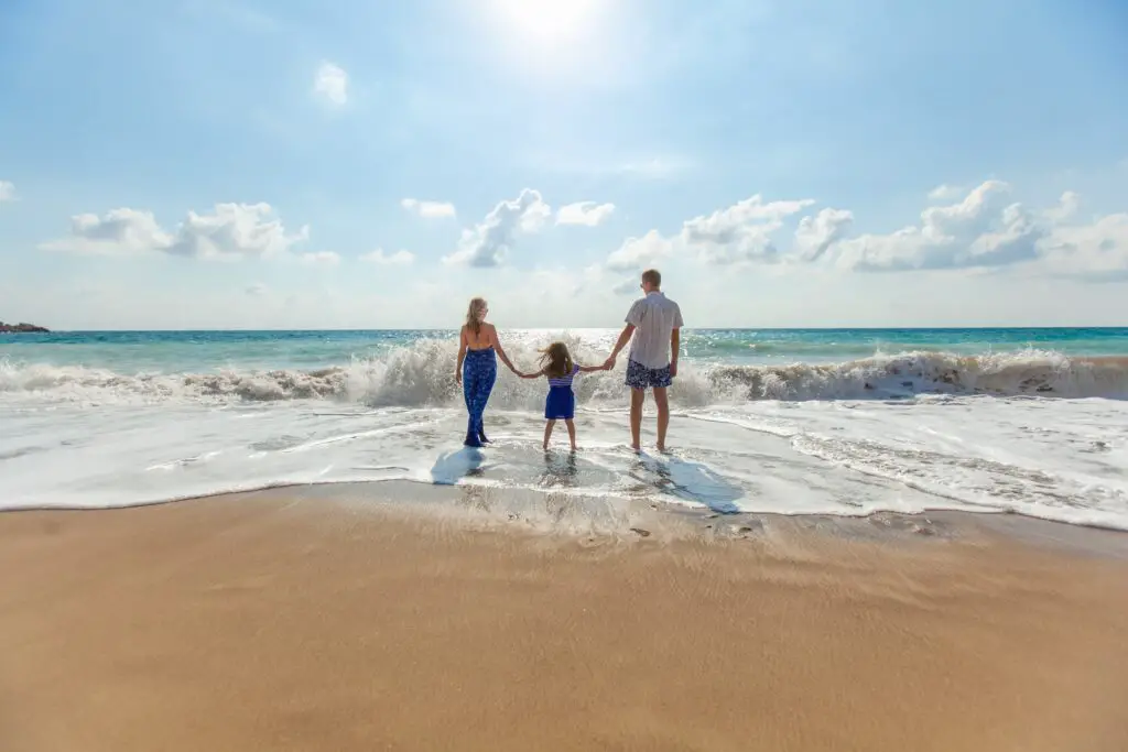 Woman, child and man stand on the shore of a beach. 